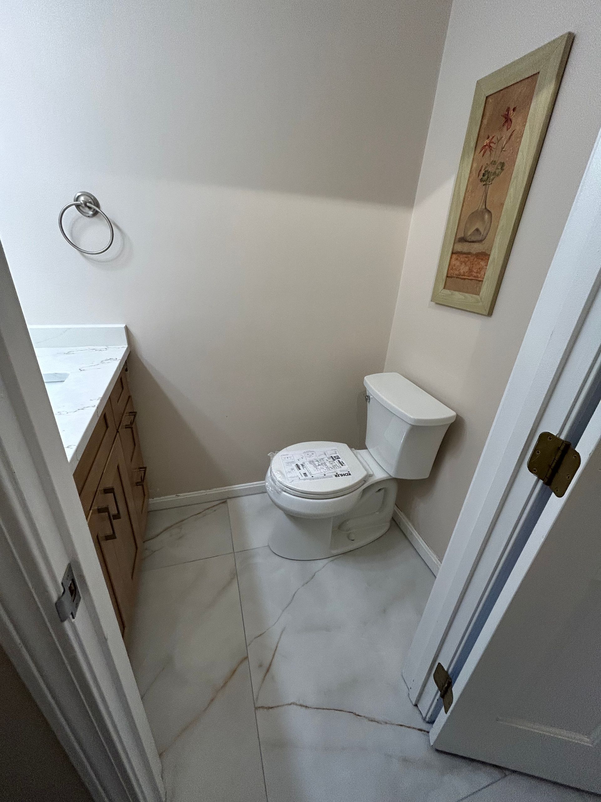 Small bathroom with a toilet, vanity, and towel ring; white walls and marble-look floor.