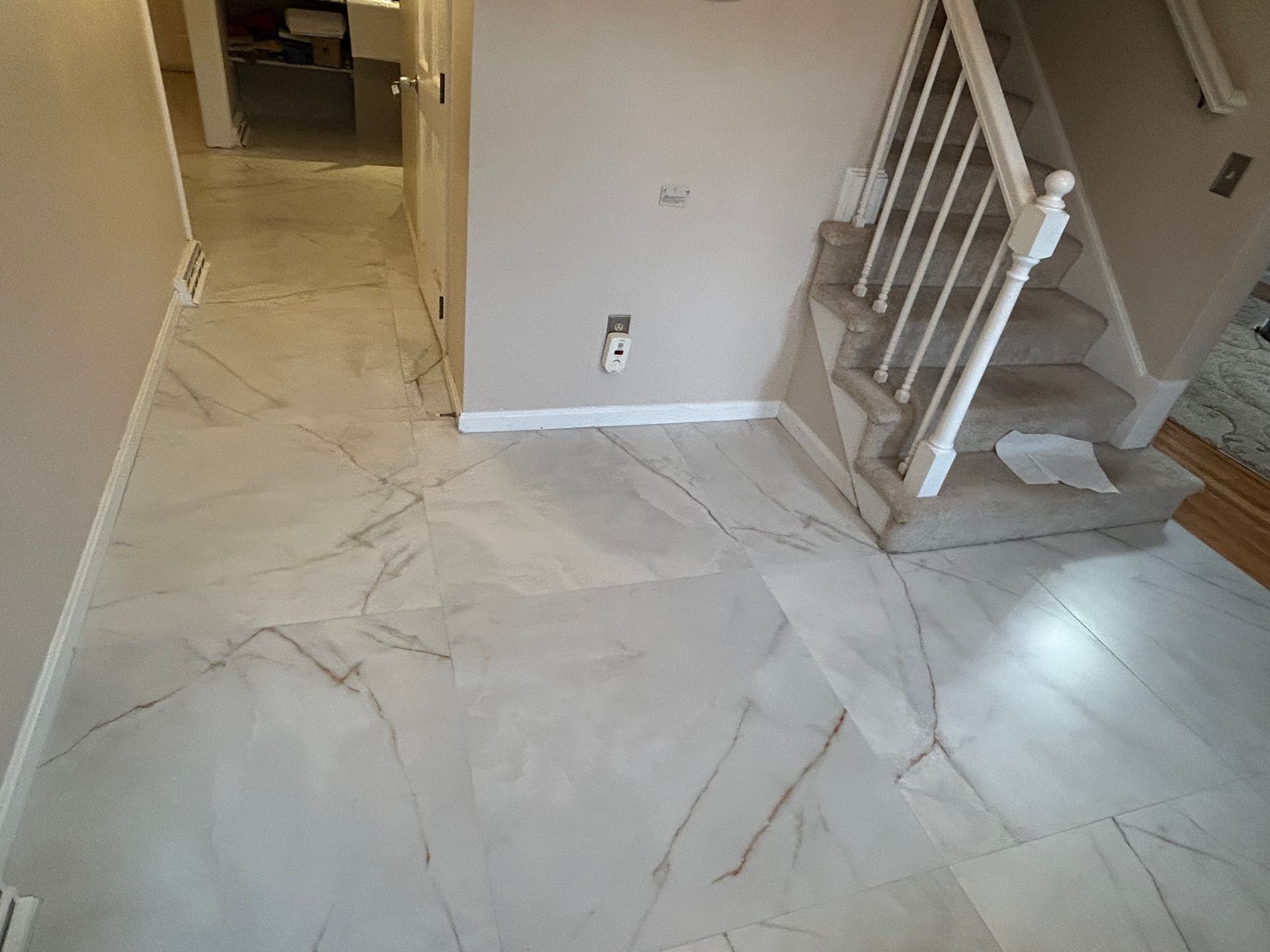 Tiled entryway with stairs, hallway, and a small outlet on the wall