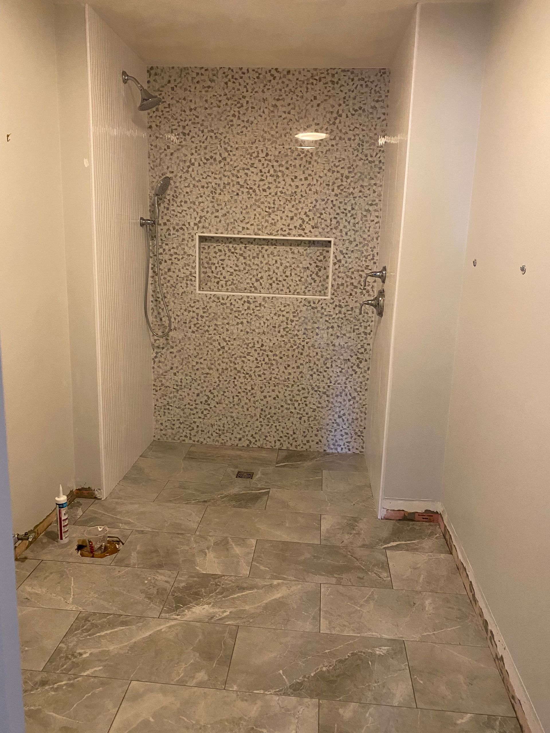 Narrow unfinished hallway with stone tile floor and mosaic-tiled shower alcove at the end