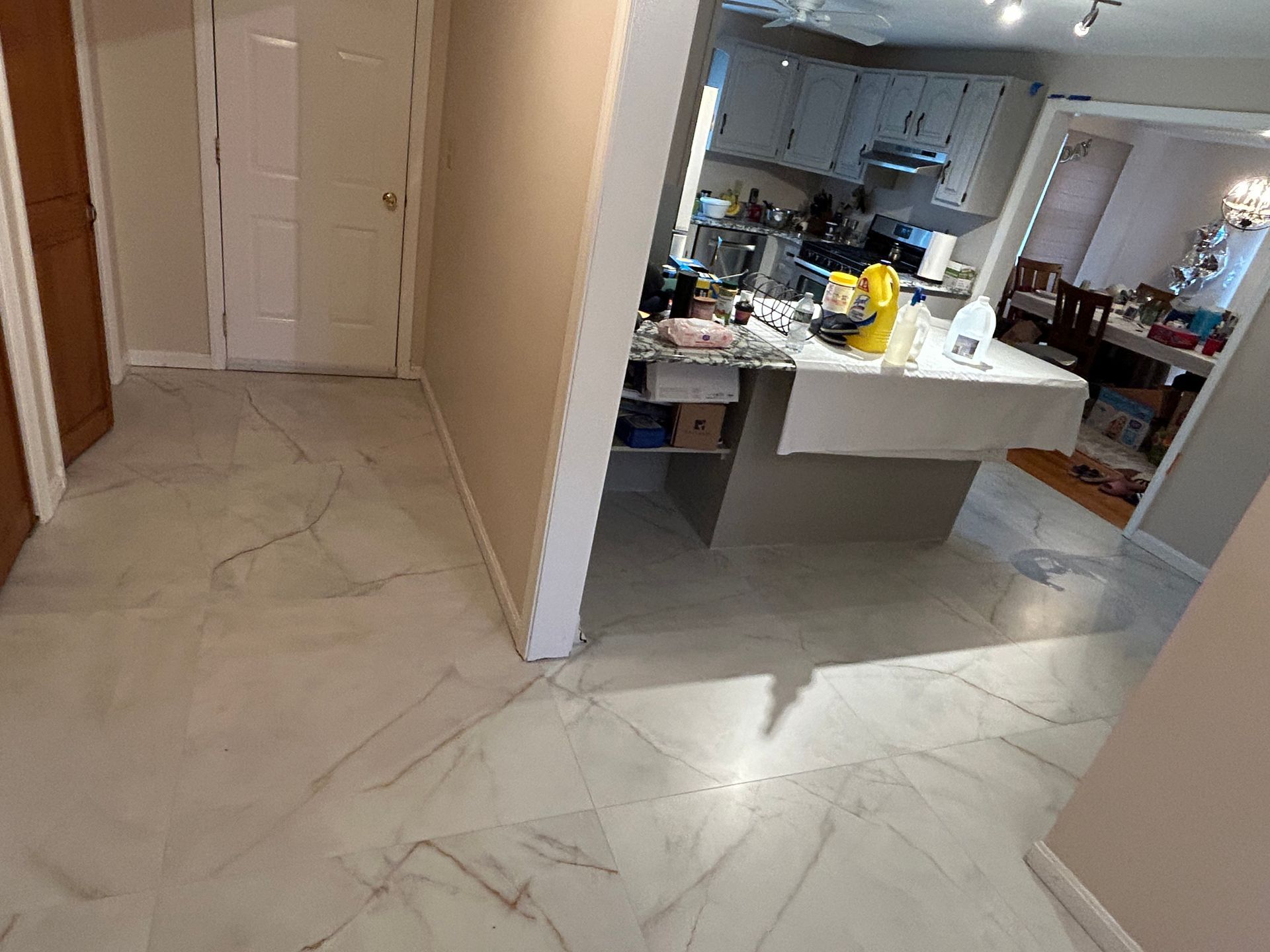 Hallway leading to a bright kitchen with a white island and marble-patterned tile floor.
