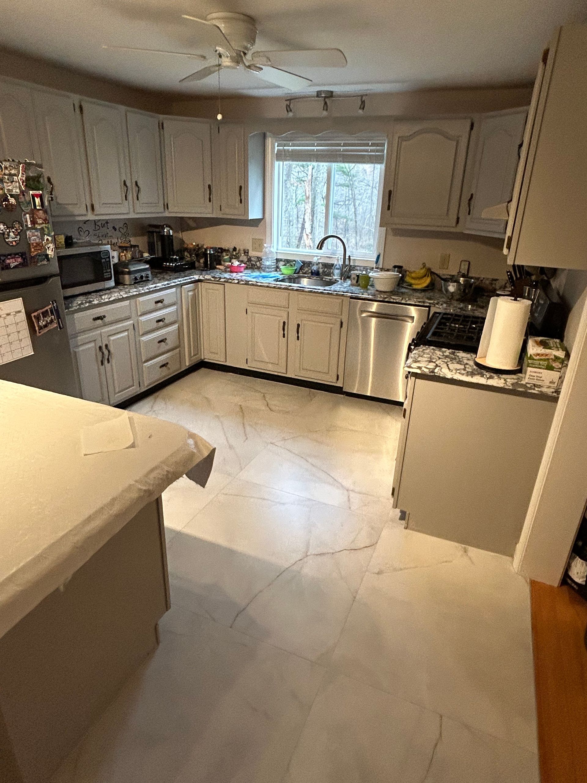 Bright kitchen with white cabinets, tiled floor, and a window over the sink.