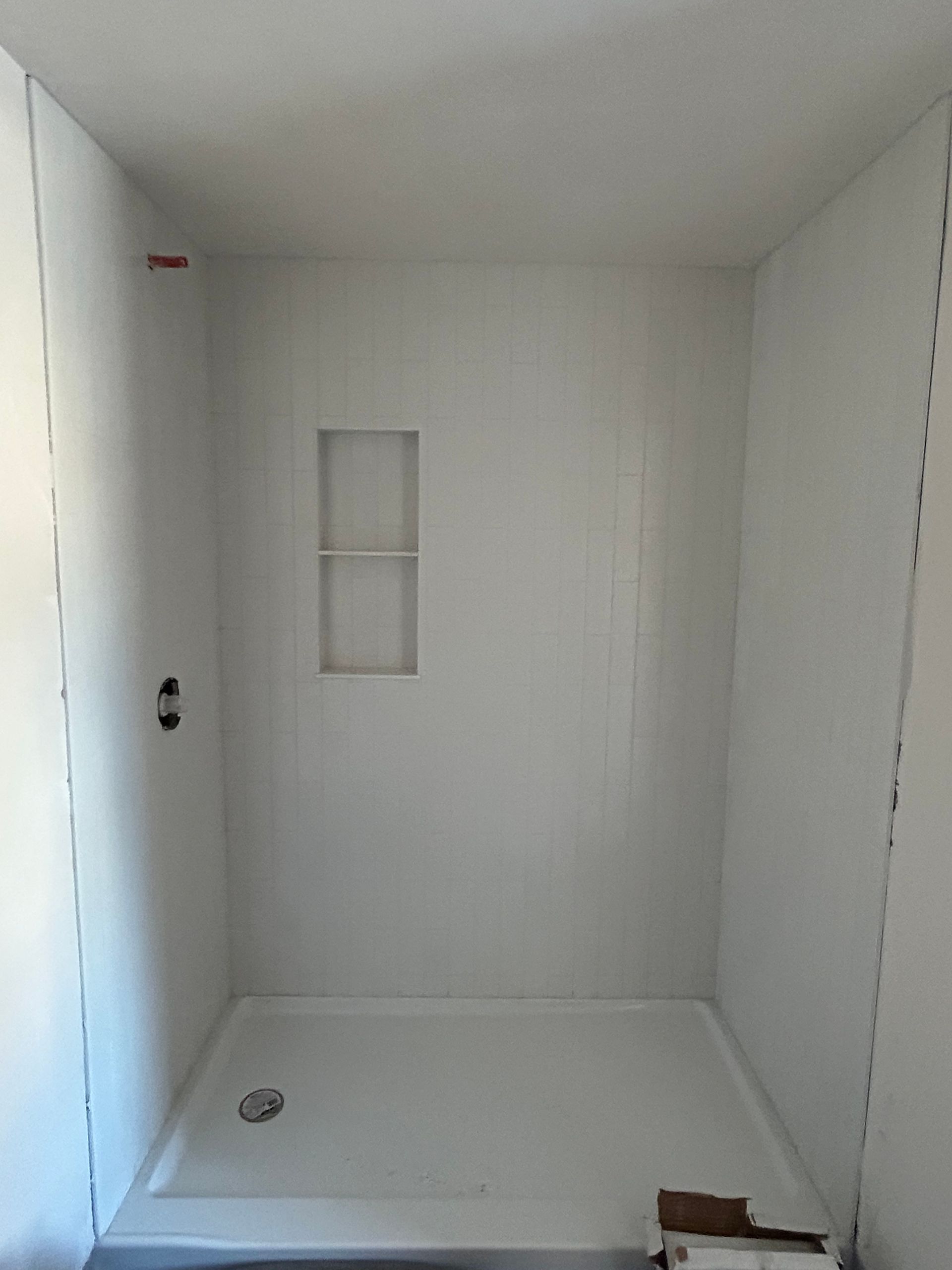 Empty white shower stall with a small window and drain near the floor