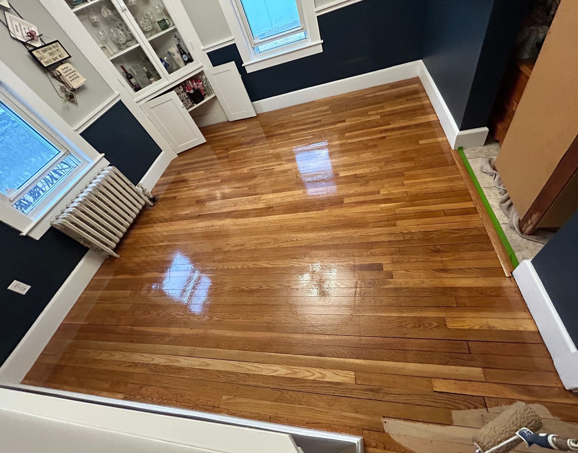 Empty room with glossy hardwood floor, dark walls, white trim, and windows along one side.