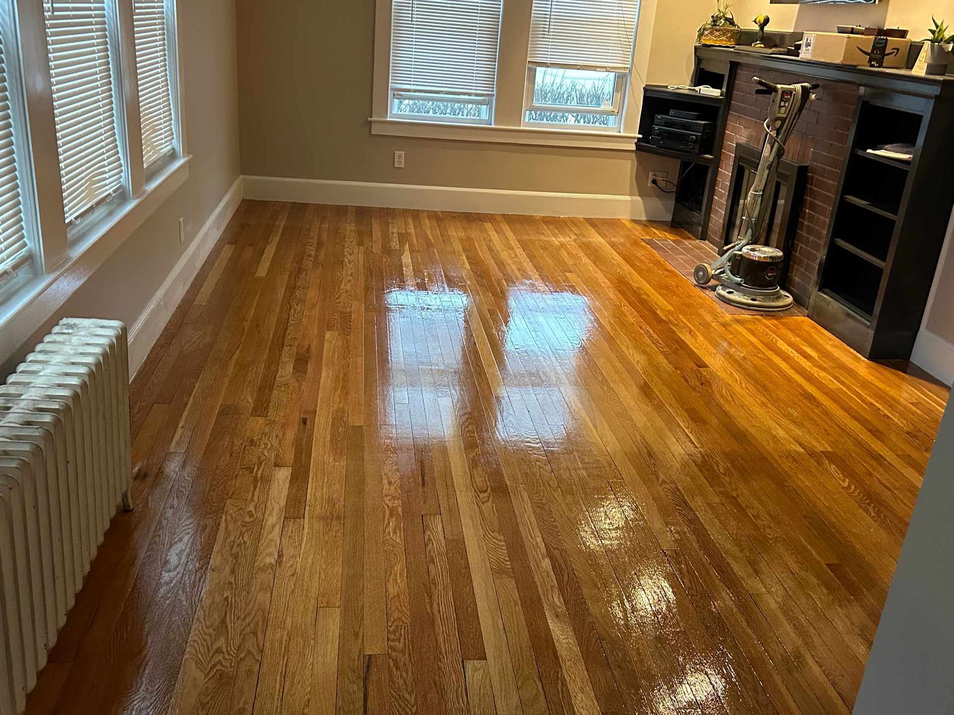 Sunlit hardwood living room with windows, fireplace, and TV stand; floor reflects light.