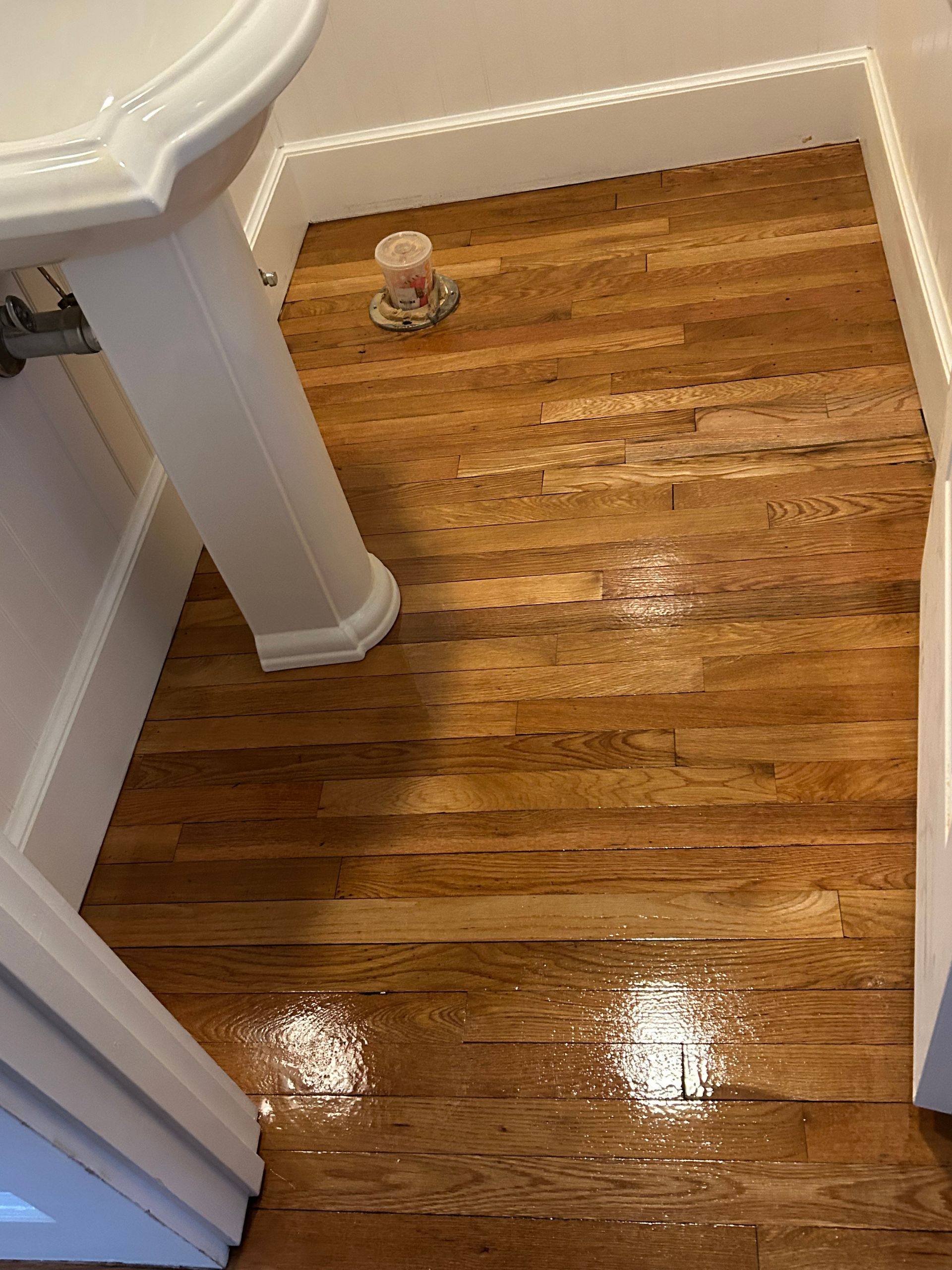 Shiny hardwood floor in a small bathroom corner with a toilet and tub visible