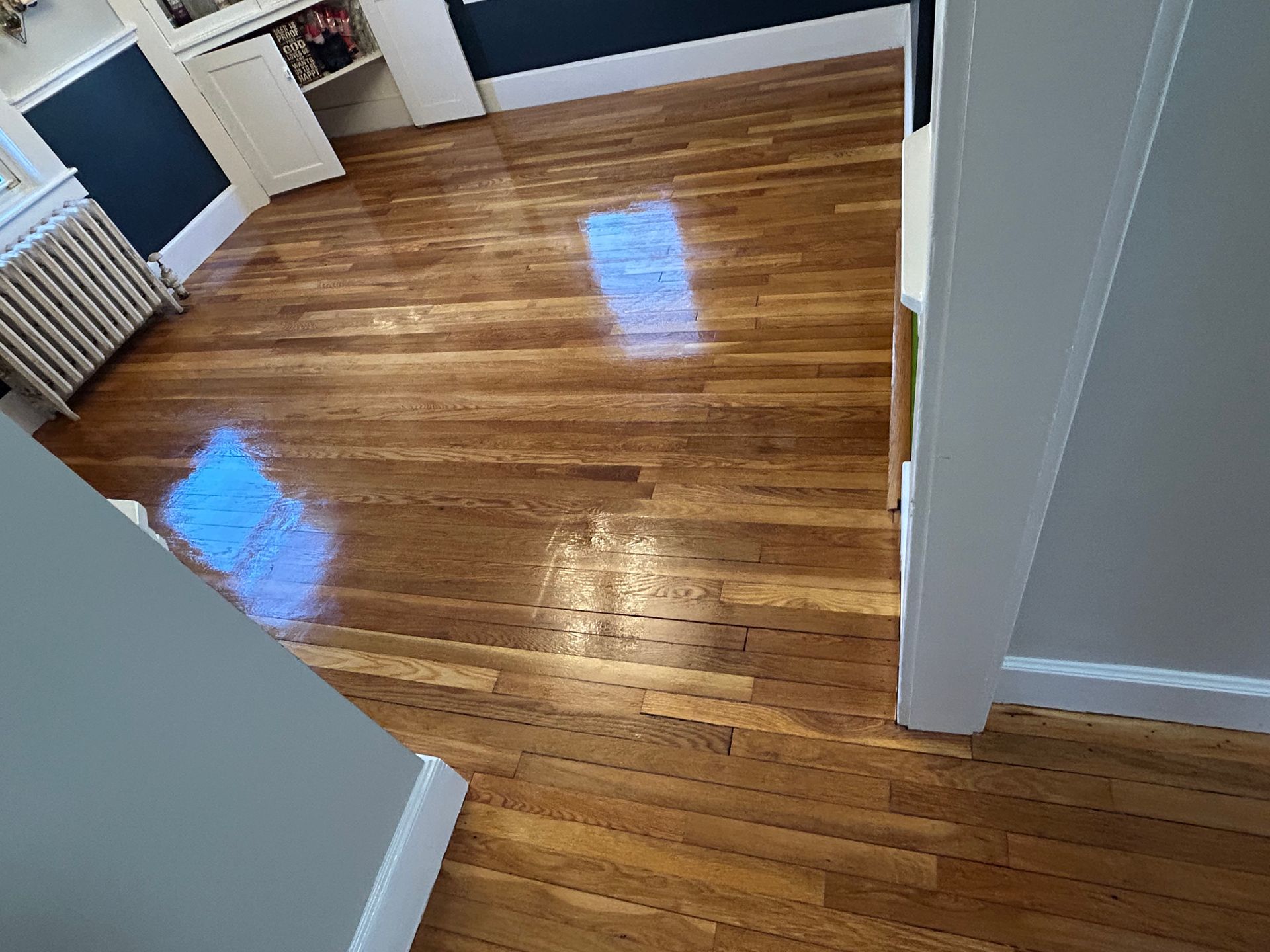 Empty room with glossy hardwood floor, white walls, and a radiator by the window.
