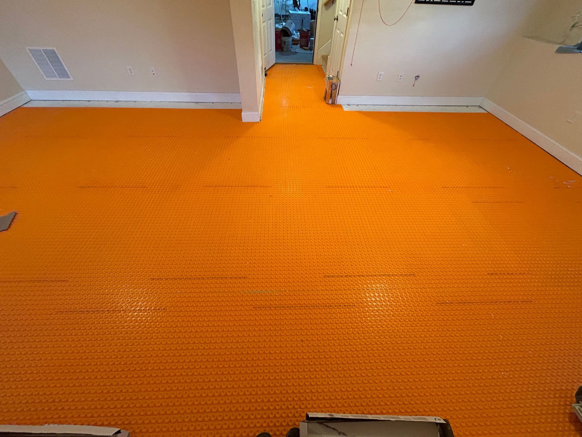 Orange carpet laid across a room floor, leading into a hallway with white walls and doorways.