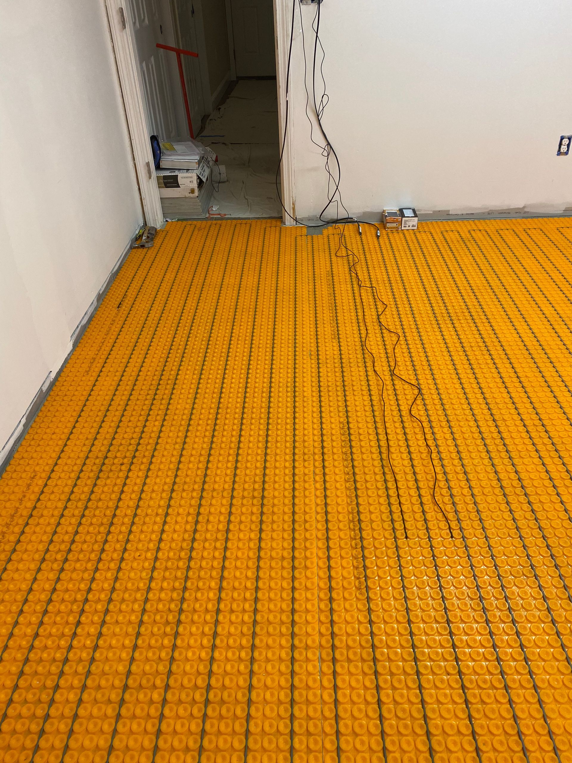 Orange underlayment flooring in an unfinished hallway with exposed wires and walls.