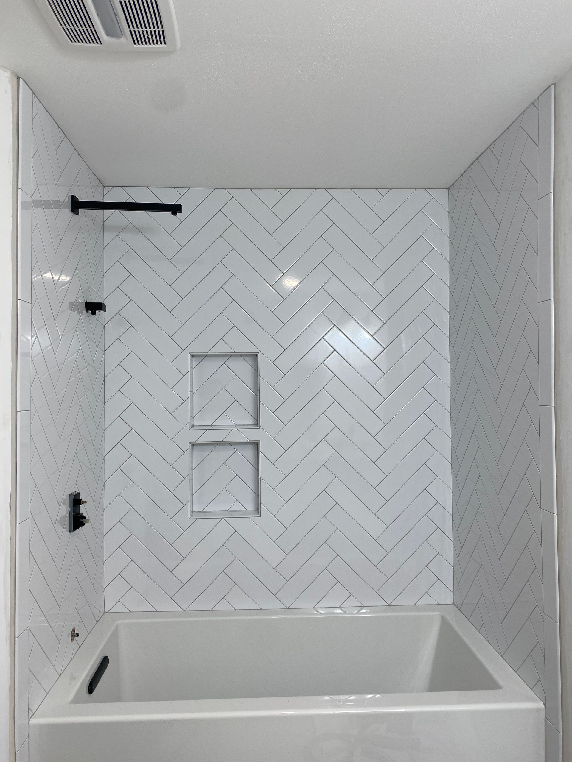 White-tiled bathroom with a tub, herringbone shower wall, and built-in niche shelves