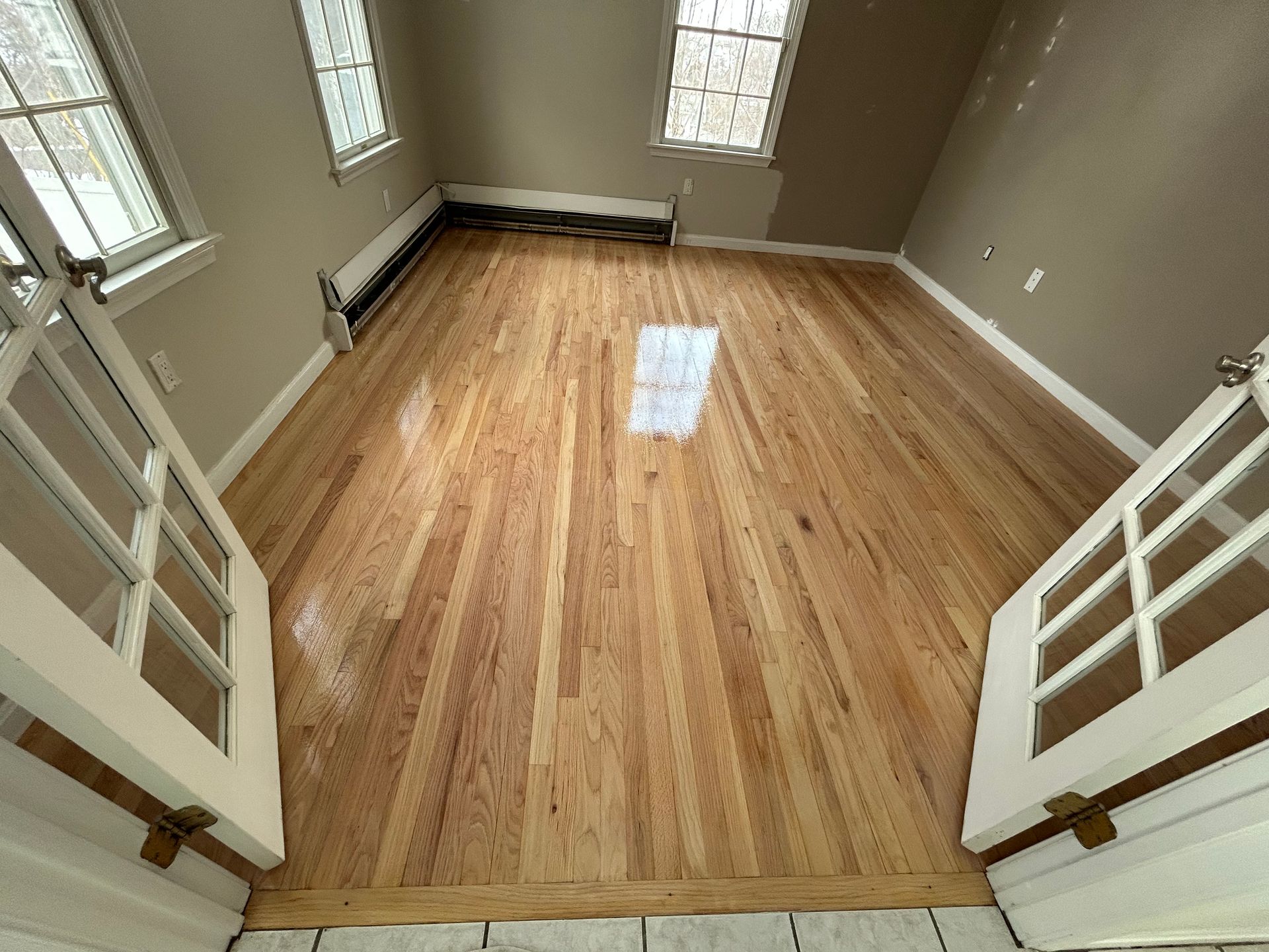Empty room with polished hardwood floors, beige walls, and windows on both sides