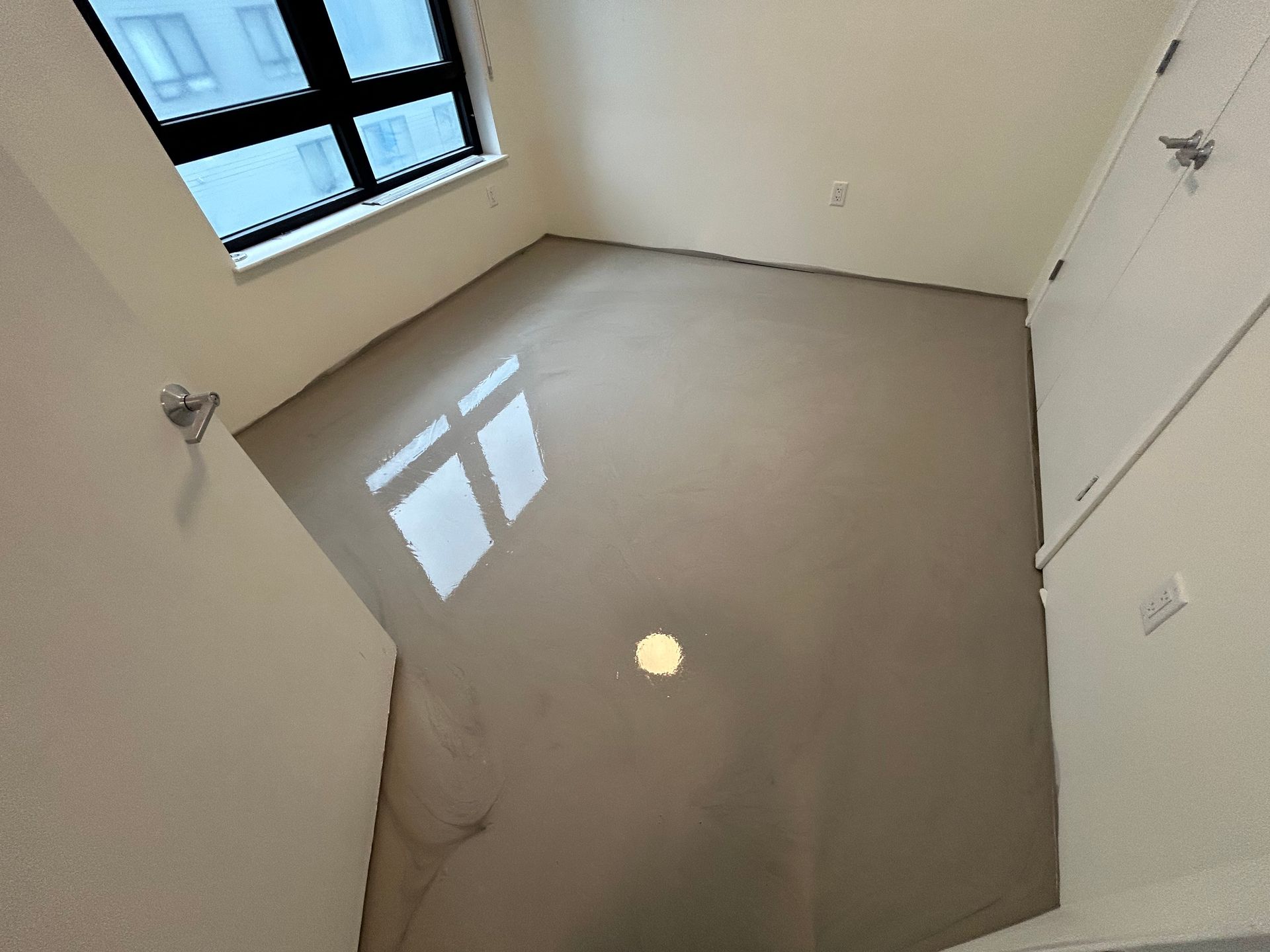 Small empty room with glossy beige floor, white walls, and a window on the left.