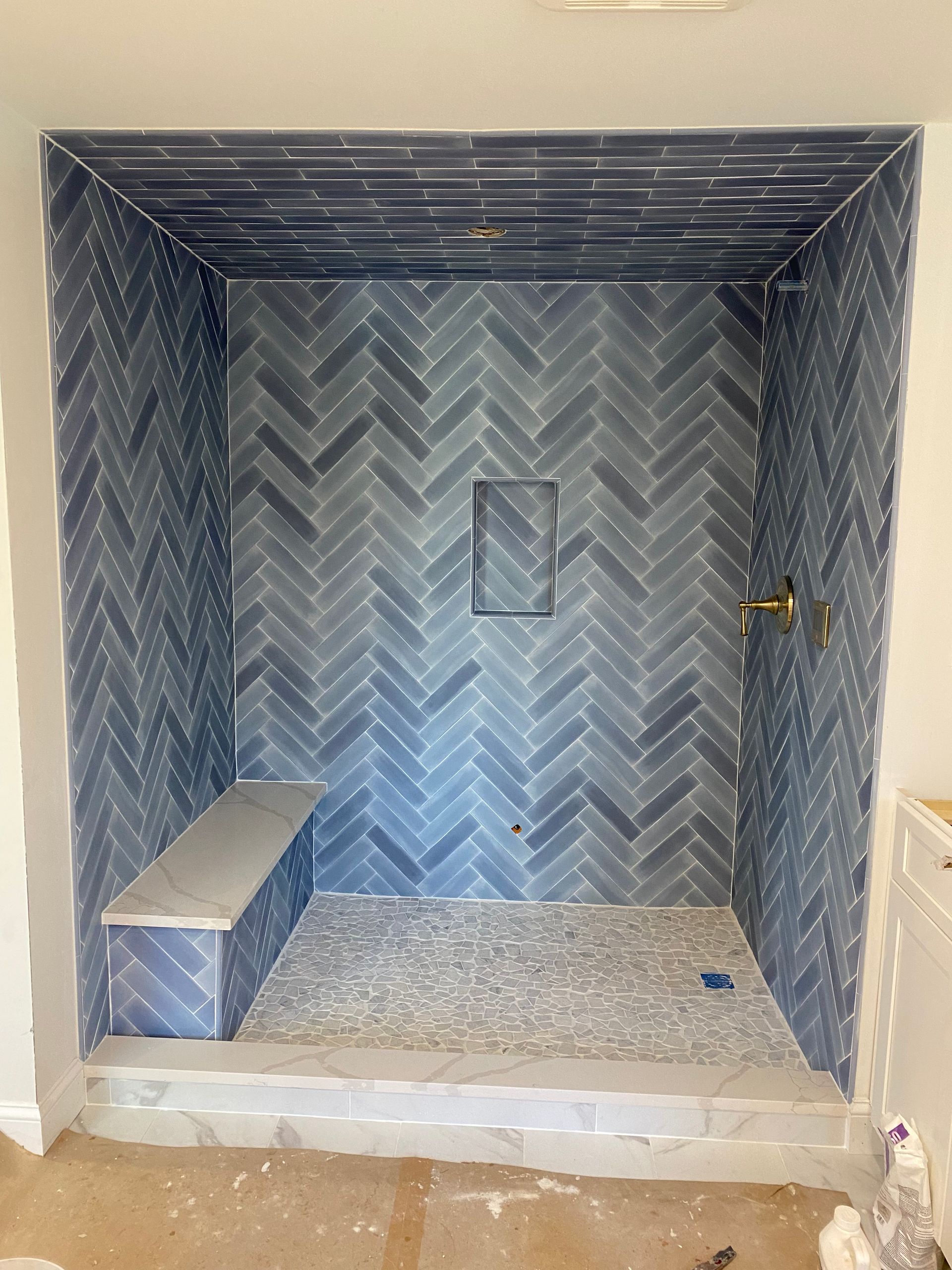 Empty tiled shower stall with chevron-patterned walls, built-in bench, and a small recessed niche.
