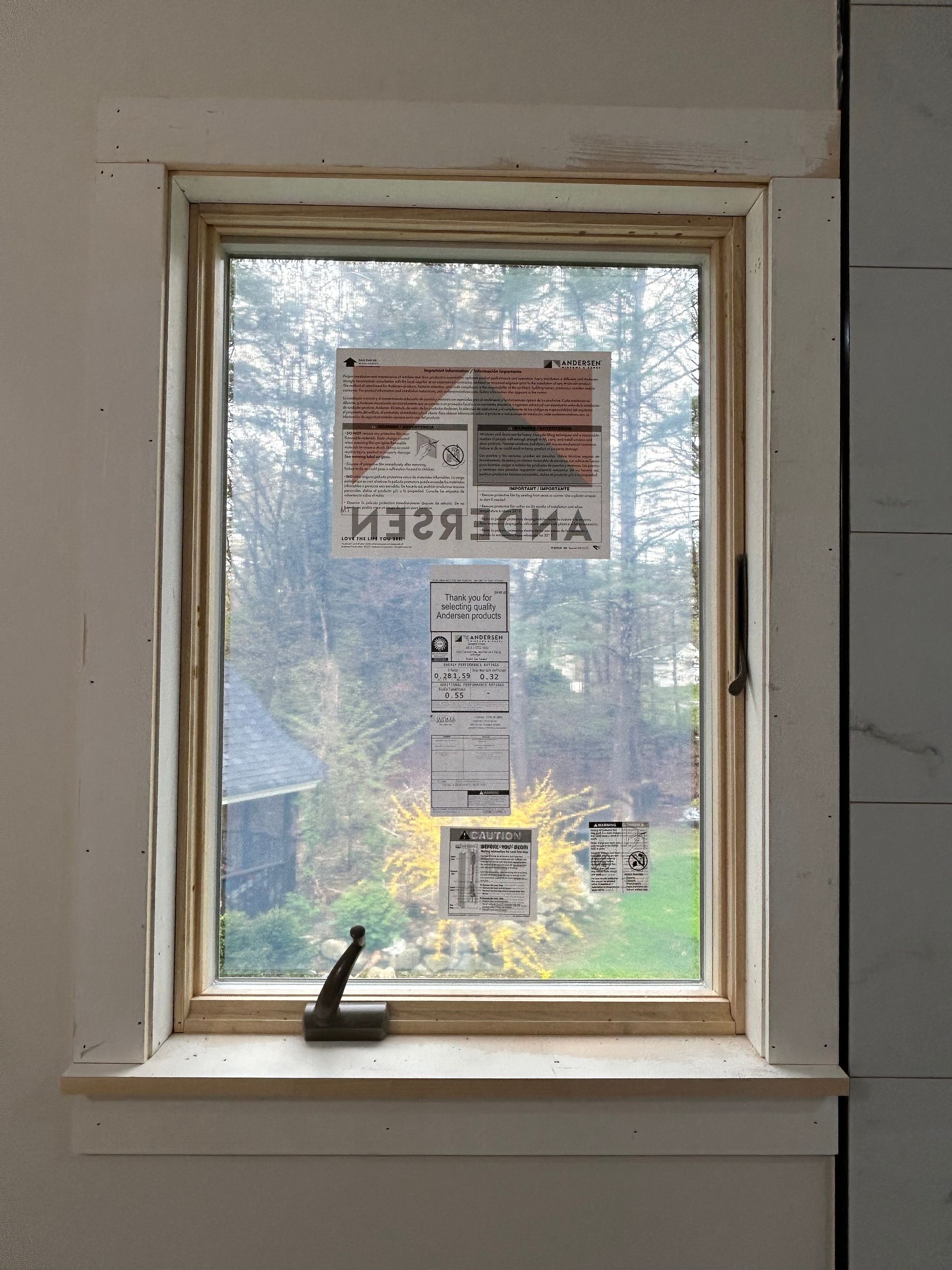Window with an “OPEN/OPENED” sign and other notices, looking out onto trees and a lake.