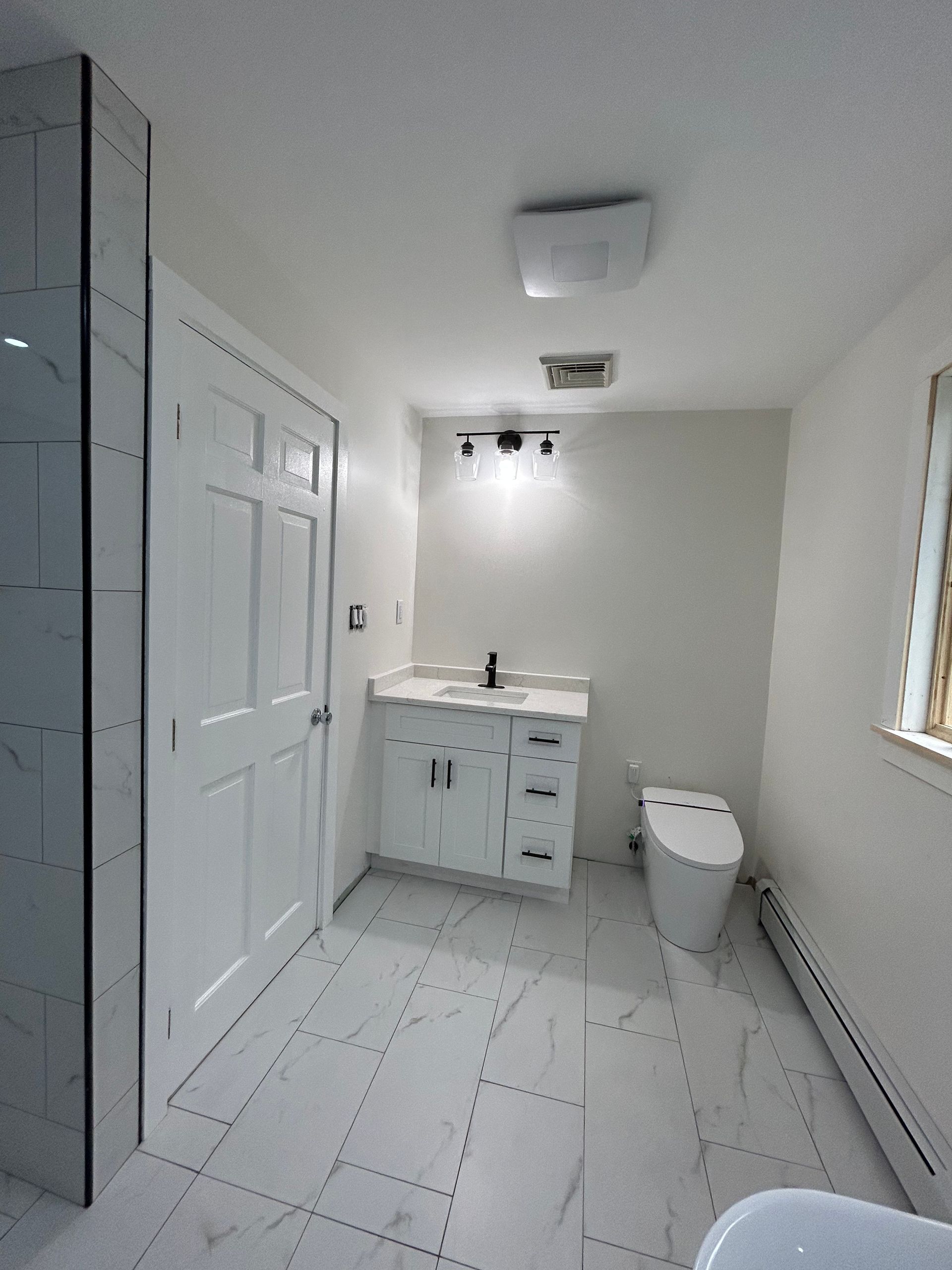 Small white bathroom with tiled floor, sink, toilet, shower, and window.