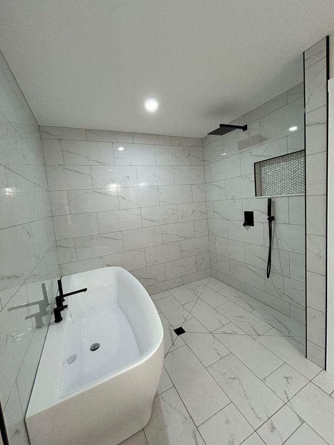 Modern white bathroom with freestanding tub, marble tile walls, and large glass shower enclosure