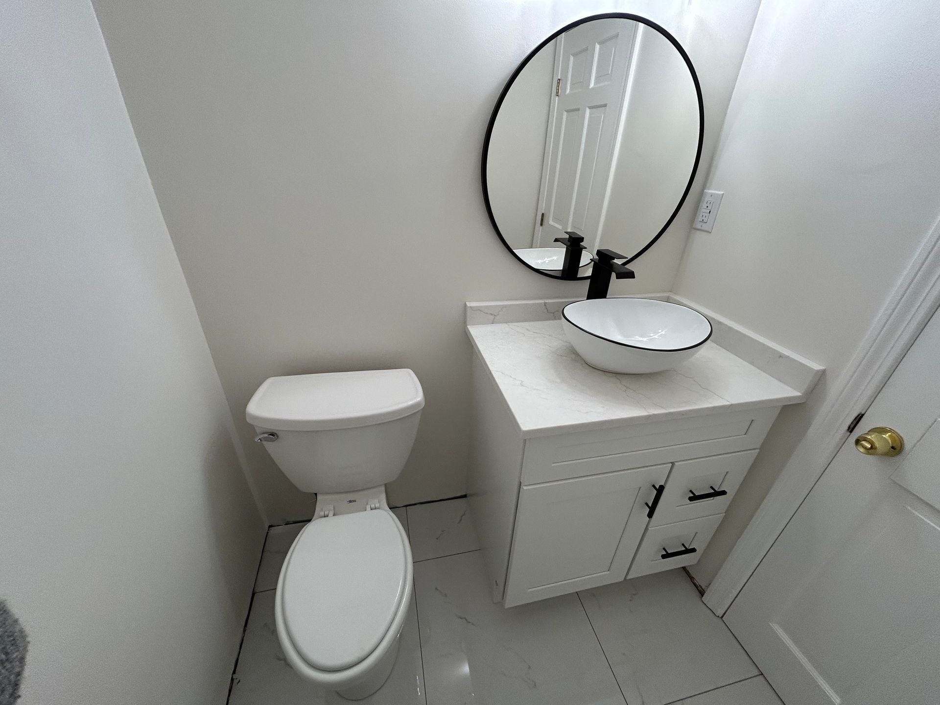 Small white bathroom with toilet, vanity sink, and round mirror