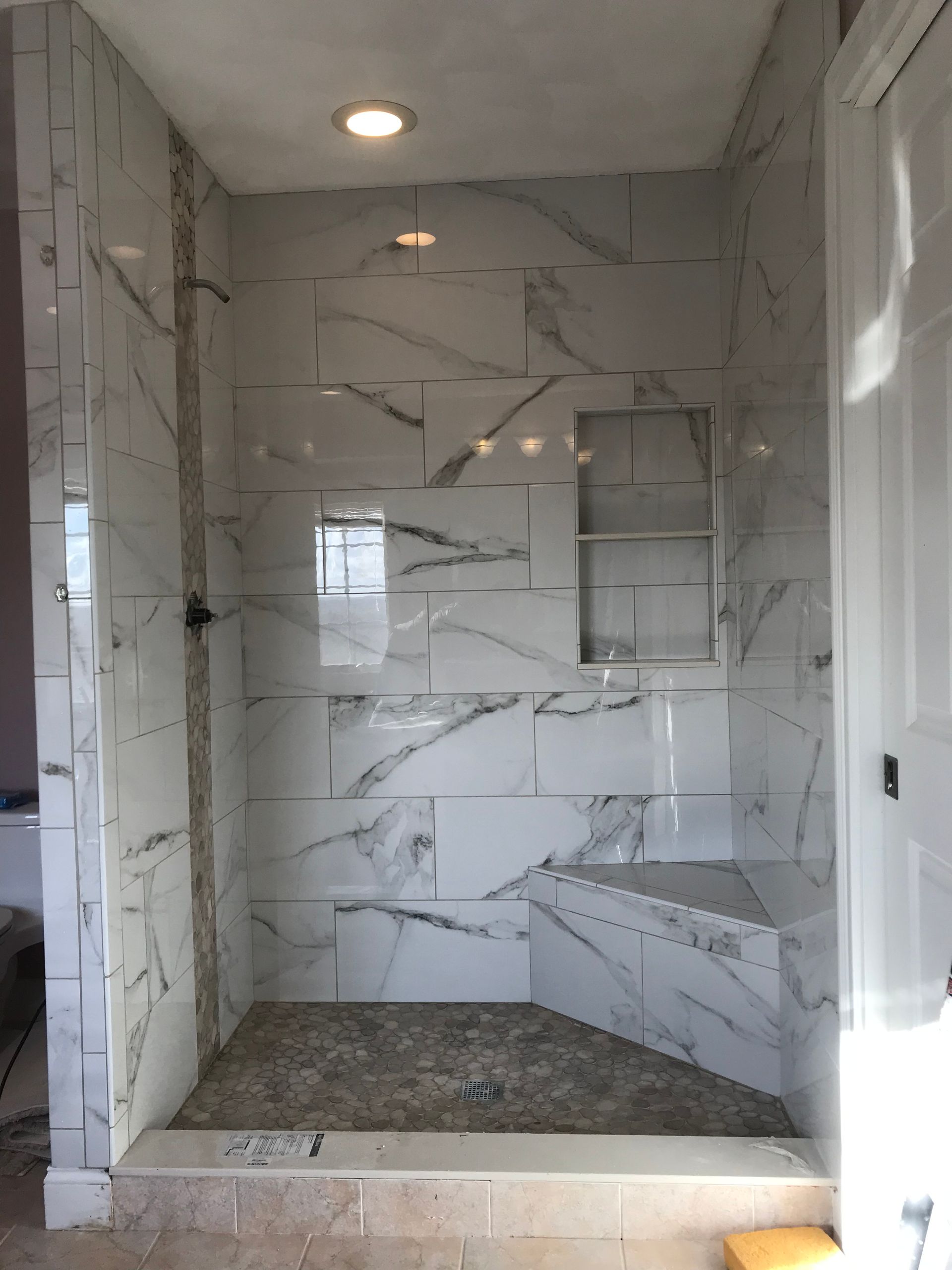 Tiled walk-in shower with marble-look walls, built-in shelf, and recessed ceiling light