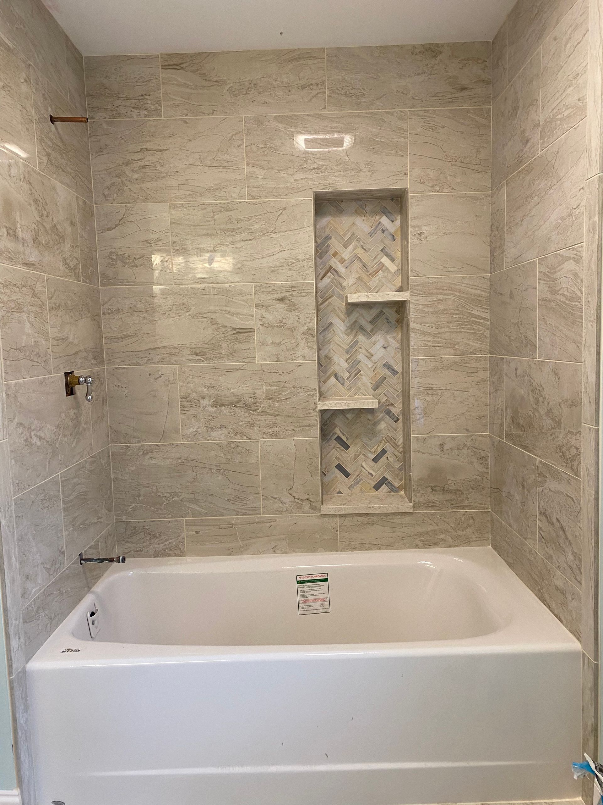 Modern bathroom with white bathtub, beige stone tile walls, and built-in shower shelf niche.