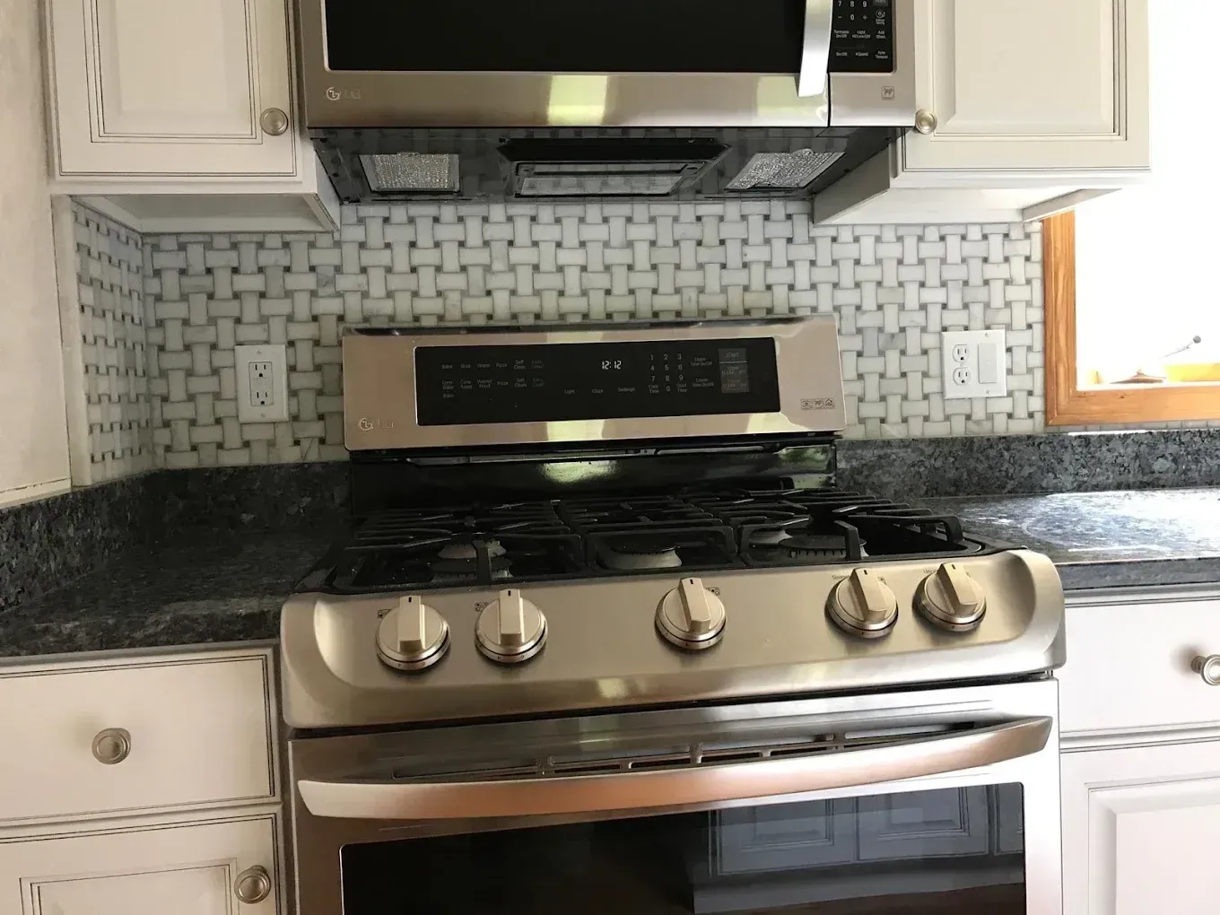 Kitchen stove with stainless steel oven, black cooktop, and white cabinets with gray mosaic backsplash
