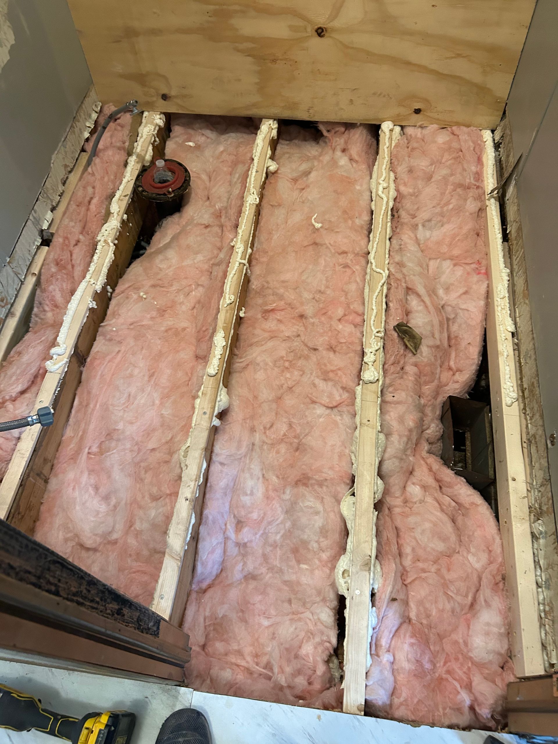 Open ceiling cavity with pink fiberglass insulation between wooden joists and exposed wiring.