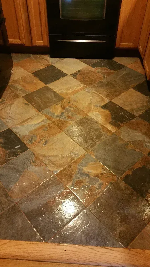 Tiled kitchen floor with multicolored diamond-patterned stone tiles near a black oven and wood cabinets