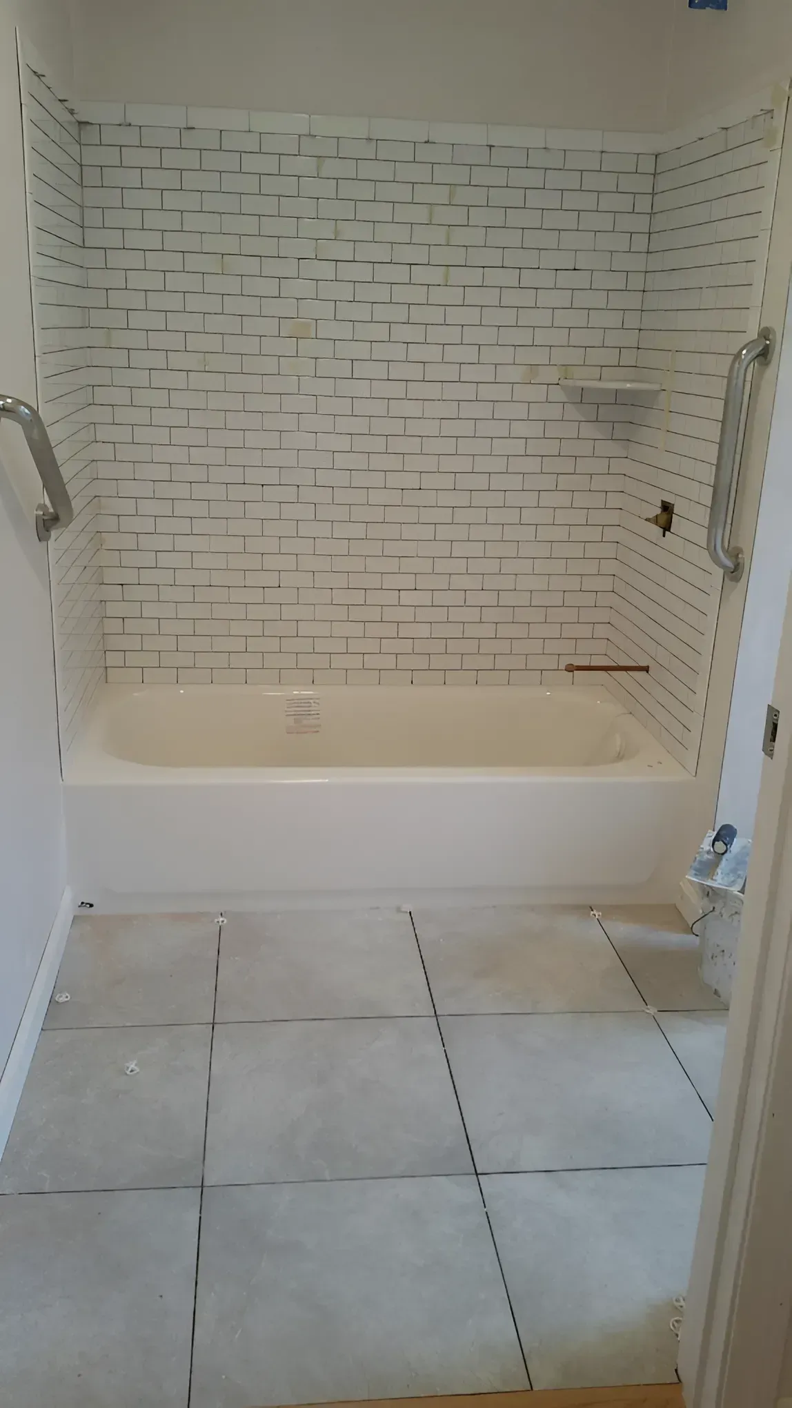 Empty bathroom with a white tub, subway tile shower wall, and large gray floor tiles.