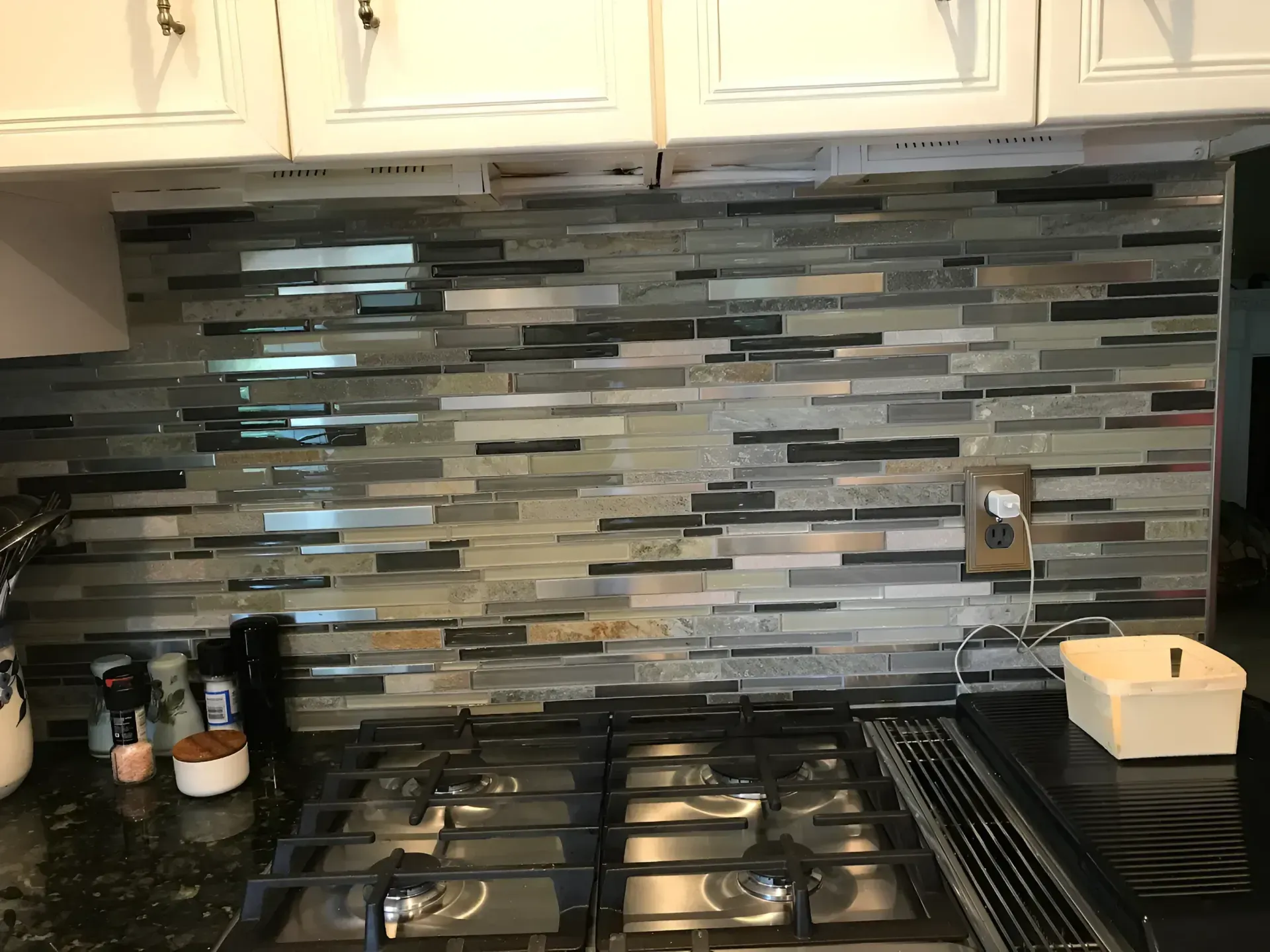 Kitchen stove with stainless burners and a gray tile backsplash under white cabinets