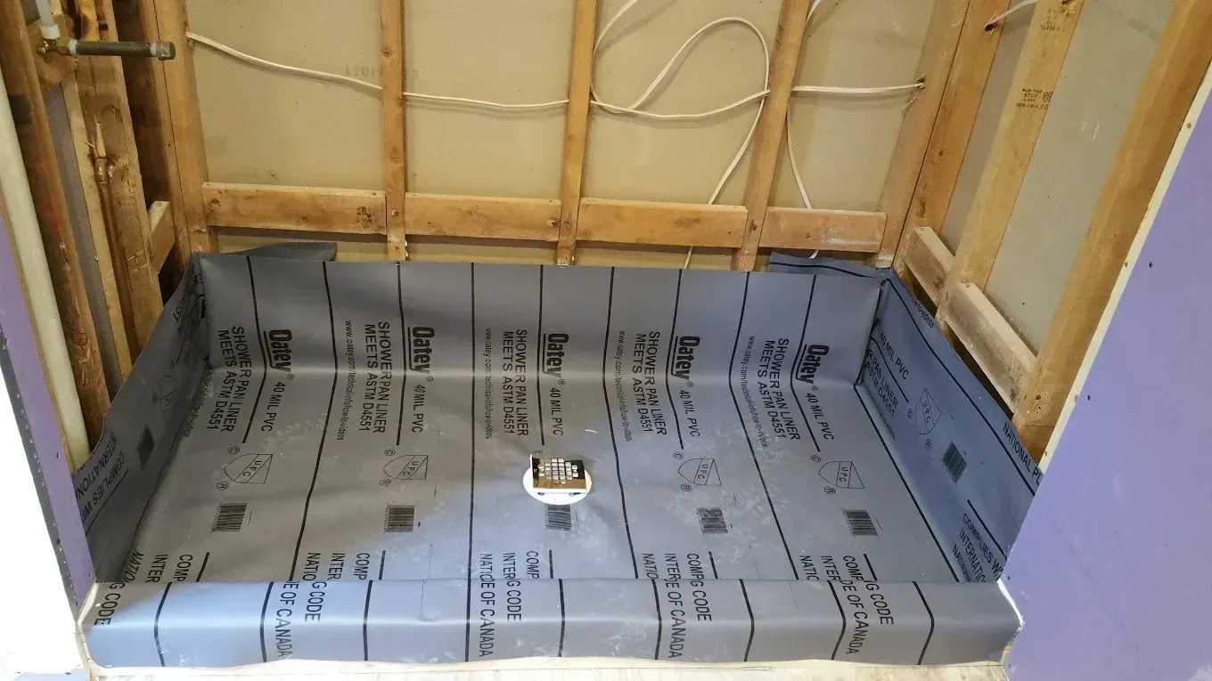 Small unfinished wooden enclosure lined with blue waterproof membrane and a drain hole in the center.