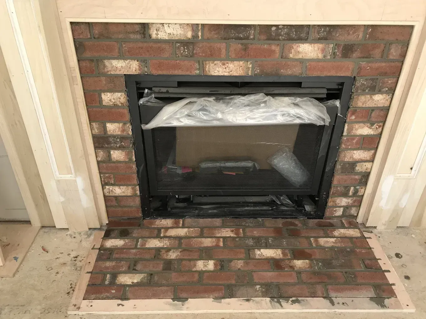Brick fireplace with black glass insert, surrounded by a brick hearth and white trim.