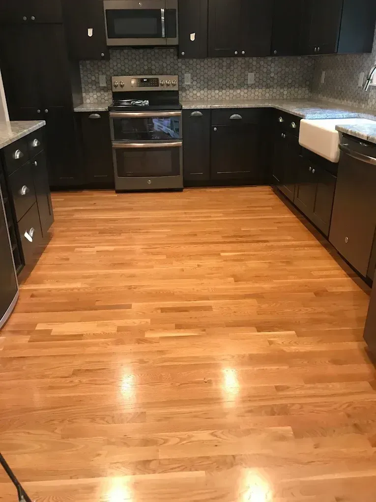 Modern kitchen with hardwood floor, dark cabinets, stainless steel appliances, and black-and-white counters.