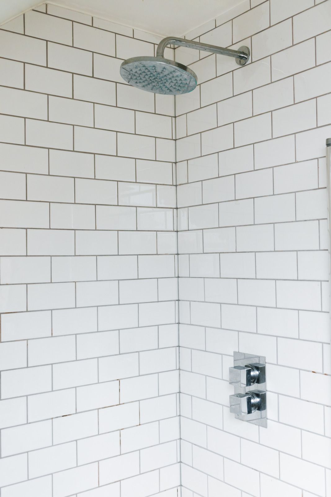 Small gray tiled shower stall with a pebble floor and built-in shelf.