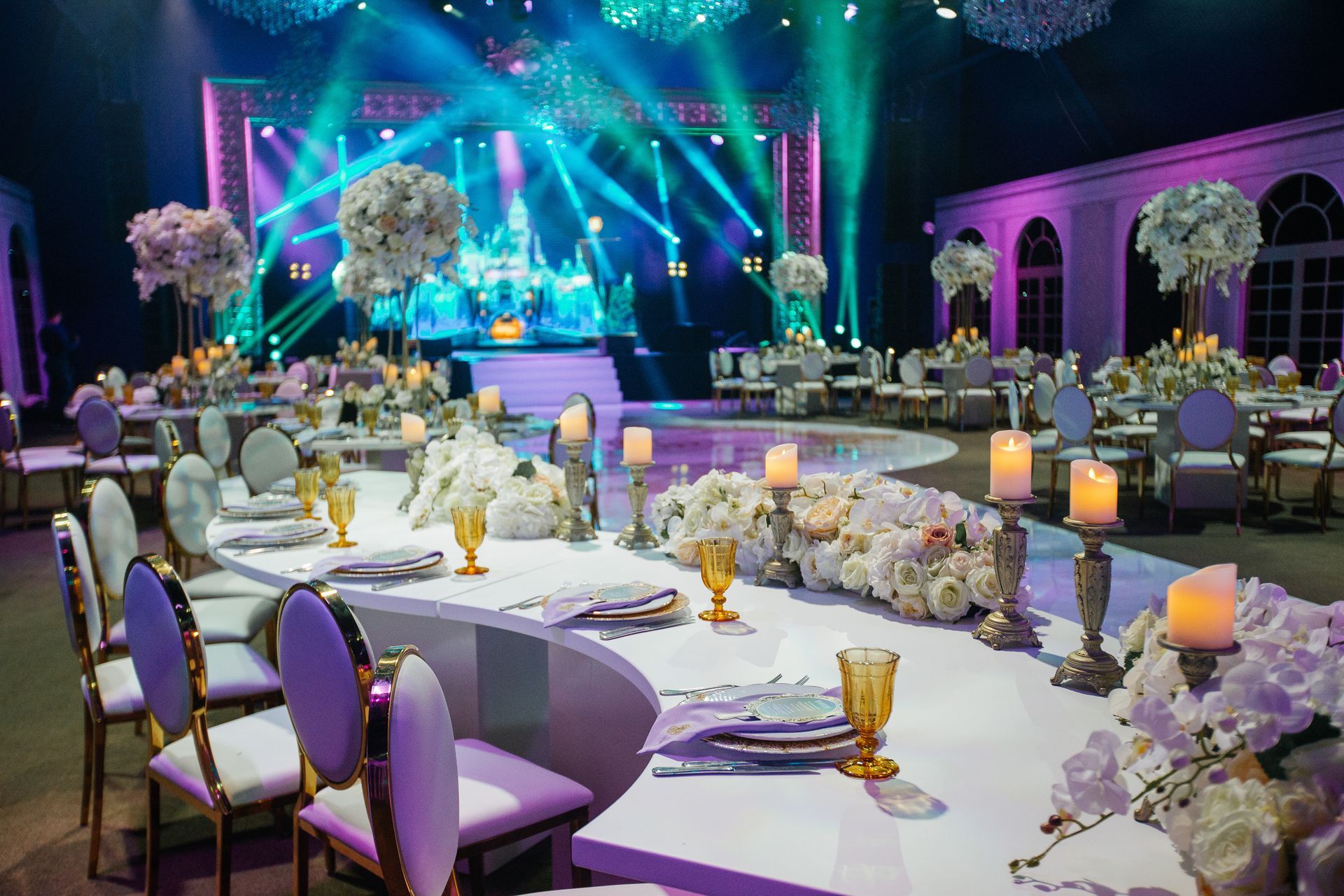 Elegant banquet hall with round tables, white floral centerpieces, and a blue-lit stage for an event