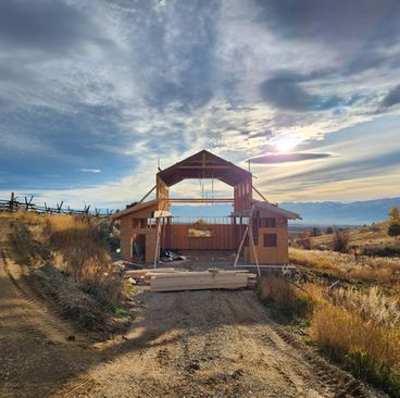 Partially built wooden house under construction in a rural field at sunset