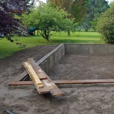 Wooden planks laid as a makeshift ramp over a concrete pit in a grassy park.