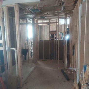 Interior of a house under renovation, with exposed framing, drywall, and construction debris in a hallway.