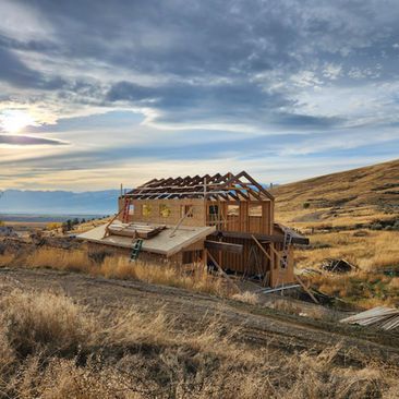 Partially built wooden house in a dry grassy field at sunset under a cloudy sky