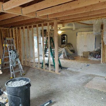 Interior under renovation with exposed studs, ladders, tools, and covered furniture on a dusty floor
