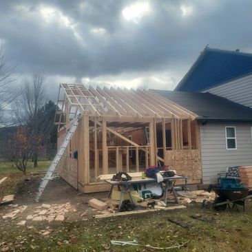 Partially built house addition with exposed wooden framing and ladder under cloudy sky