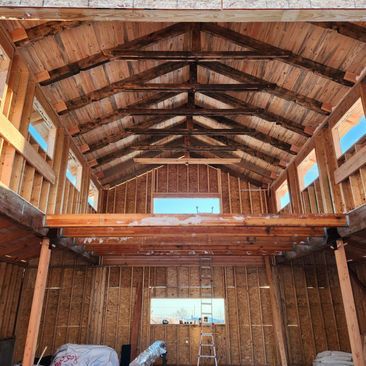 Interior of a rustic wooden barn under construction, with exposed beams and open windows.