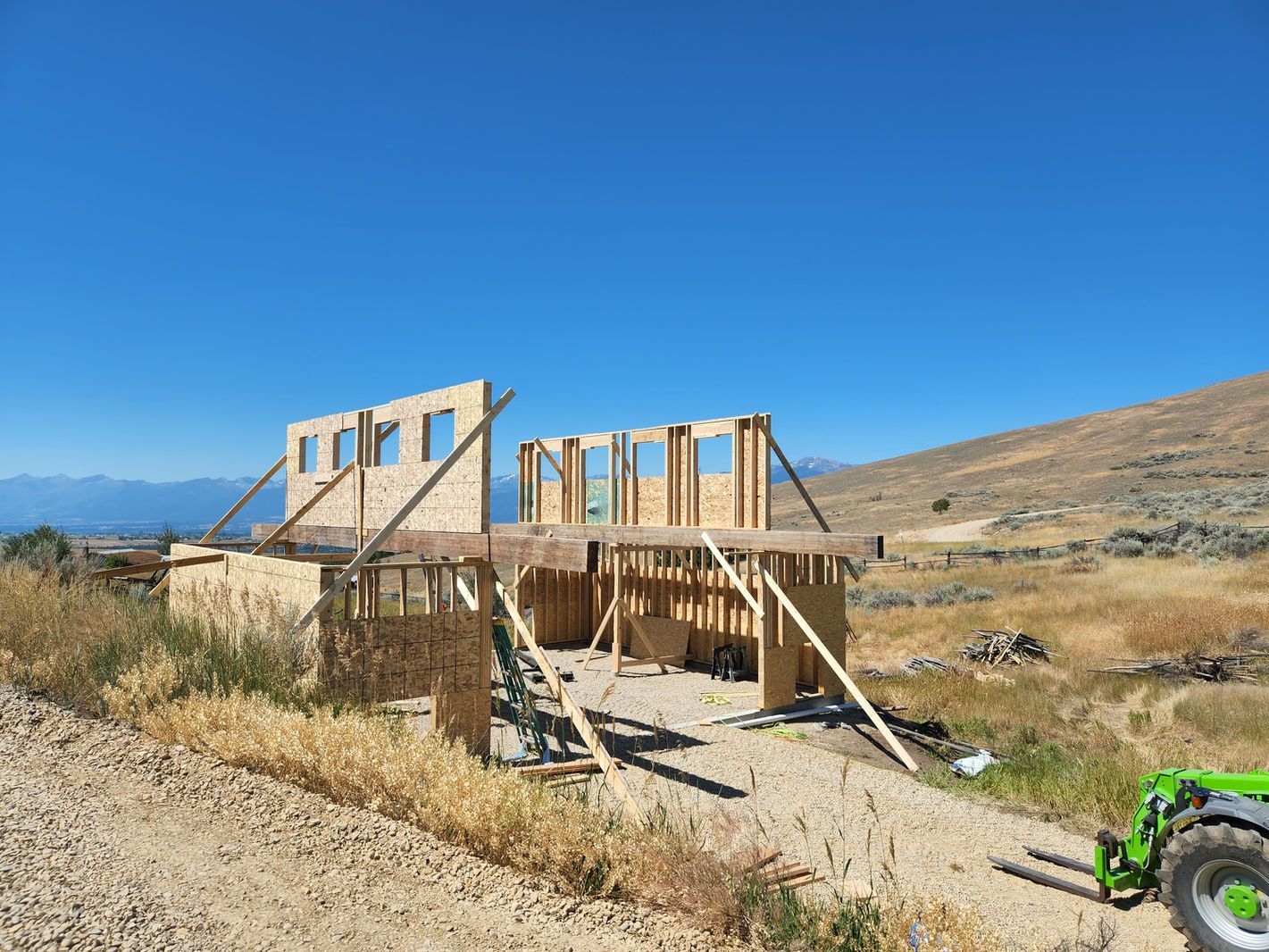 Wood-framed house under construction in a dry, rural landscape with a blue sky