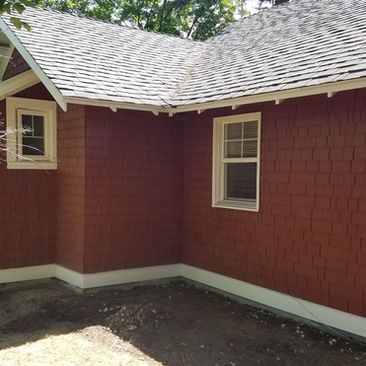 Red house exterior with white-trim windows and gray shingled roof over a dirt yard corner