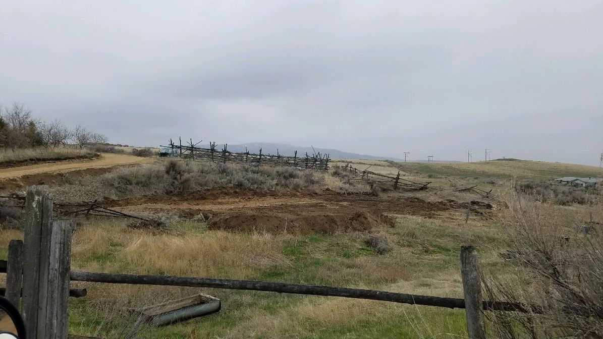 Grassy hillside under a gray sky, with a weathered wooden fence in the foreground