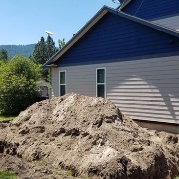 Large dirt pile beside a blue house with beige siding in a sunny yard