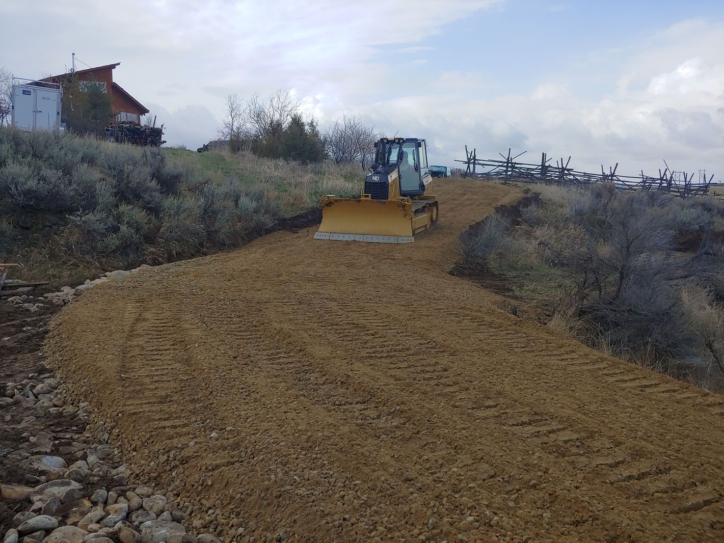 Yellow bulldozer grading a dirt path on a hillside under a cloudy sky
