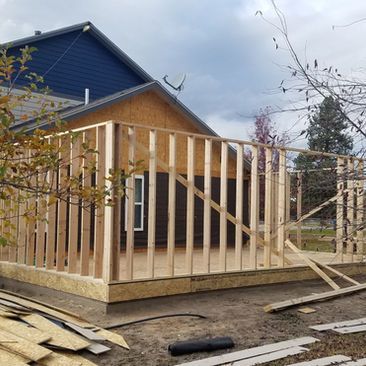 Wood-framed house under construction with exposed studs and blue siding in the background