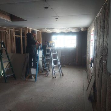 Renovation site with two ladders and a worker in a dim room with exposed walls and bright window.