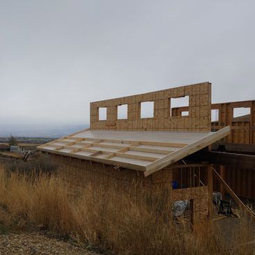 Partially built wooden house with sloped roof in a dry, overcast rural landscape