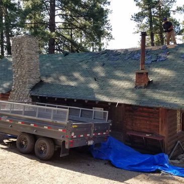 Truck parked beside a cabin roof under repair, with tarps and a worker on the roof.