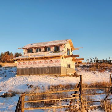 Snow-covered rural house at sunset with a wooden fence under a clear blue sky