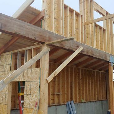 Wood-framed house under construction with exposed beams, plywood sheathing, and temporary supports